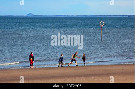 Portobello Promenade, Édimbourg, Écosse, Royaume-Uni. 11 avril 2020. Température de 16 degrés avec plein soleil dans l'après-midi après un début nuageux. Le samedi de Pâques, une plage très calme le troisième week-end de coronavirus Lockdown. Une famille s'amuse au bord de la mer. Banque D'Images