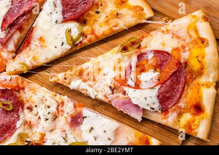 Pizza maison en tranches avec pepperoni et fromage sur un panneau de découpe en bois de fermeture. Banque D'Images