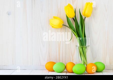 Bouquet de tulipes jaunes et œufs de pâques multicolores sur panneaux en bois clair, fond de planches en bois. Maquette Paschal avec espace de copie. Espace vide pour te Banque D'Images