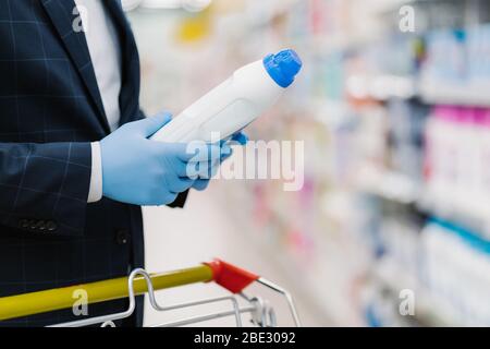 L'homme choisit un détergent dans la boutique de produits ménagers, tient une bouteille avec de la poudre liquide, porte des gants médicaux pour se protéger du coronavirus, lit l'infor du produit Banque D'Images