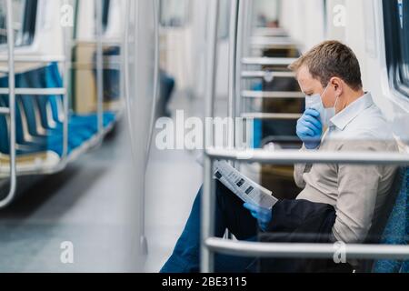 Interdiction de la libre circulation. L'homme en vêtements formels, tousse et a des symptômes de coronavirus, porte un masque médical de protection et des gants, lit le journal Banque D'Images