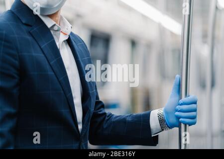 Le passager de l'homme porte un gant médical protecteur du coronavirus, touche la main courante dans le chariot de métro, pose dans les transports publics, habillés officiellement. Virus Banque D'Images