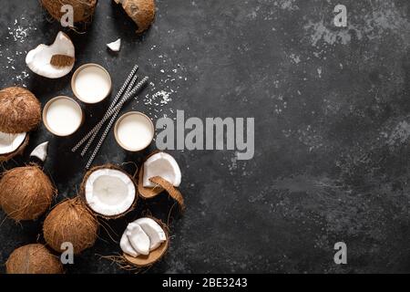 Lait de coco, noix de coco entières et fissurées sur fond noir, vue de dessus Banque D'Images