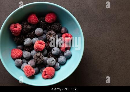 un magnifique bol bleu clair de fruits avec framboises, bleuets et mûres sur fond noir anthracite, vue de dessus, studio tourné Banque D'Images