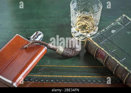 Flasque de hanche, verre de whisky, pipe en bois, livre vieux, table en cuir vert. Concept. Étude de gentleman, relaxation, nostalgie, propre compagnie, seule Banque D'Images