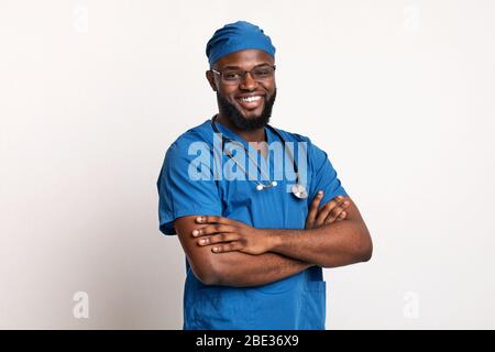 Jeune chirurgien noir en uniforme bleu souriant sur blanc Banque D'Images