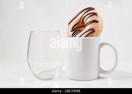 Pas de verre à vin à tige se rafraîchit à côté d'un mug à café blanc de 11 oz. La tasse à café contient un beignet tentant. Banque D'Images