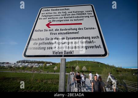 Dortmund, Allemagne. 11 avril 2020. Un panneau rappelle aux visiteurs du lac Phoenix d'utiliser le chemin circulaire dans le sens horaire seulement, afin de contenir la propagation du coronavirus en gardant une distance de sécurité avec d'autres personnes. Le lac artificiel sur le site d'une ancienne aciérie est l'une des destinations récréatives les plus fréquentées de la ville. Crédit: Bernd Thissen/dpa/Alay Live News Banque D'Images