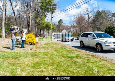 Une famille reconnaissante debout sur leur pelouse avant et se réveille à tout le monde dans la promenade d'anniversaire heureux-en célébrant leur fils pendant COVID-19. Banque D'Images