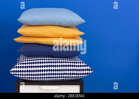 Pile de coussins sur une table de nuit en bois contre un mur intérieur bleu Banque D'Images
