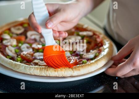 Pizza maison avec légumes. Le processus de fabrication de pizza à la maison. Mains de femmes qui font de la pizza et brossant les bords de la croûte avec de l'huile d'olive. Banque D'Images