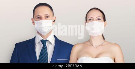 Meilleur jour de vie. Mariage pendant la période du coronavirus. Mariée et marié dans des masques médicaux de protection posant sur un fond gris Banque D'Images