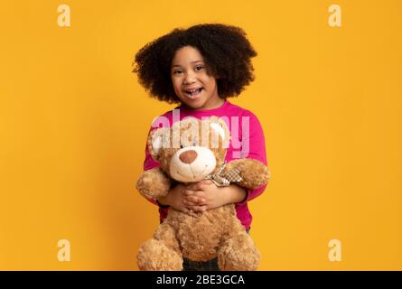 Bonne fille noire avec grand ours en peluche sur fond jaune Banque D'Images