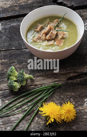 Délicieuse soupe de brocoli crémeuse végétalienne avec croûtons de pain faits maison, servie dans un bol placé sur un bureau rustique en bois avec décoration de brocoli, ciboulette Banque D'Images