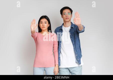 Jeune couple asiatique debout sur fond gris, faisant signe stop Banque D'Images