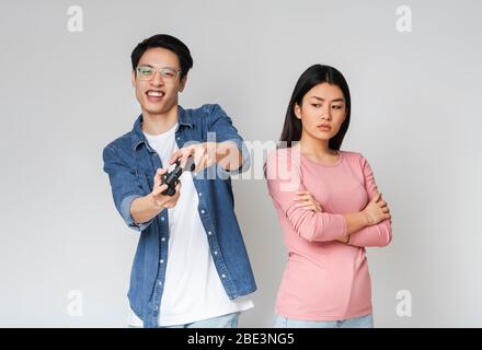 Un gars asiatique qui joue à des jeux vidéo alors que sa petite amie se sent solitaire Banque D'Images