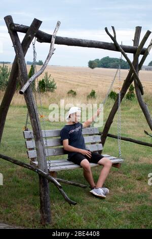 Un jeune garçon polonais reposant et bien pensé sur un balancement rustique fait maison dans sa cour. Zawady Gmina Rzeczyca Pologne Banque D'Images