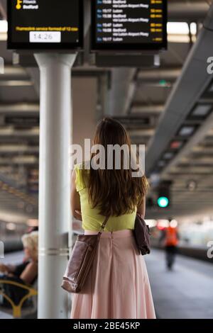 Une jeune femme étudie le panneau des arrivées à la gare de Blackfriars à Londres, en Angleterre, au Royaume-Uni. Banque D'Images