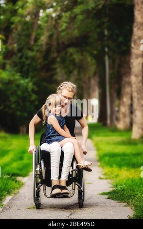 Une mère paraplégique tenant sa petite fille sur ses genoux tout en la prenant pour une promenade dans la rue son fauteuil roulant dans un après-midi d'été chaud Banque D'Images