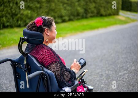 Femme maorie avec paralysie cérébrale en fauteuil roulant descendant un trottoir; Wellington, Nouvelle-Zélande Banque D'Images