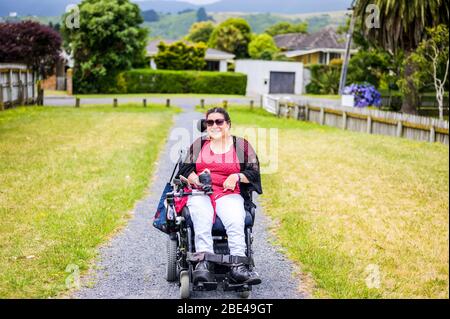 Femme maorie avec paralysie cérébrale en fauteuil roulant descendant un trottoir; Wellington, Nouvelle-Zélande Banque D'Images