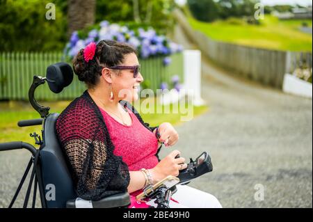 Femme maorie avec paralysie cérébrale en fauteuil roulant descendant un trottoir; Wellington, Nouvelle-Zélande Banque D'Images