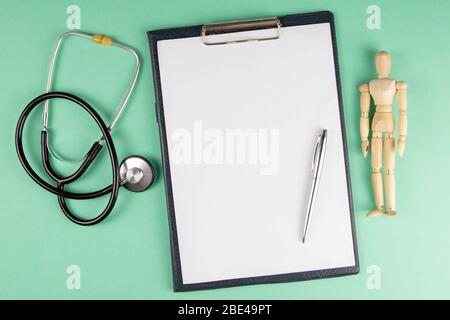 Tablette, figurine d'un homme en bois et stéthoscope sur fond vert clair, vue de dessus et espace pour le texte Banque D'Images