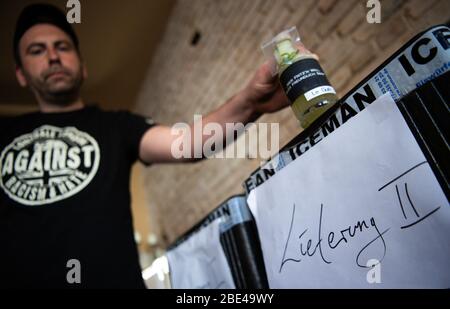 08 avril 2020, Brandebourg, Potsdam: Ronny, l'un des deux directeurs généraux du "Bar Fritz'n" à Dortustraße, place une bouteille de verre avec le cocktail "le Gurk" (gin, fleur de sureau, pomme, citron et concombre) dans une boîte de transport marquée "Delivery II". Comme les restaurants et les bars du Brandebourg sont fermés en raison du danger de Corona, une sélection de cocktails du bar Fritz'n sera livrée à l'extérieur de l'établissement. (Pour les boissons fraîches et le délicieux risotto: Pour aller au signe de Corona) photo: Soeren Stache/dpa-Zentralbild/ZB Banque D'Images