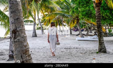 Une femme mûre marche sur le sable blanc parmi les palmiers sur une plage dans les Caraïbes, péninsule de Placencia; Belize Banque D'Images