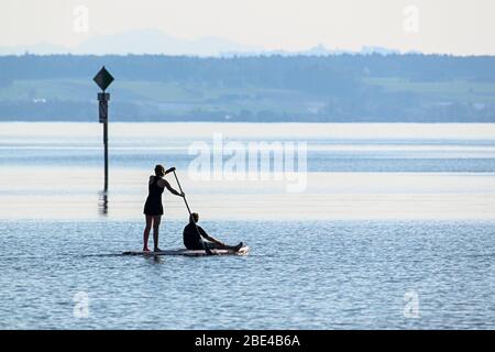 Friedrichshafen, Allemagne. 11 avril 2020. Une femme pagarade sur un plateau de paddle debout sur le lac de Constance alors qu'un enfant s'y assied à l'avant. Les ports autour du lac de Constance sont actuellement fermés. Les sorties et les travaux sur le bateau sont interdits. La pagayage debout est autorisée pendant les périodes de Corona. Crédit: Felix Kästle/dpa/Alay Live News Banque D'Images