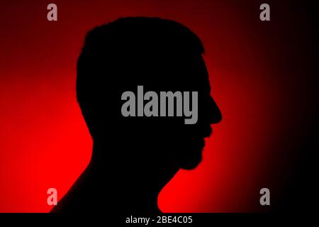Silhouette nette d'un homme sur un fond rouge avec un spot et une zone lumineuse juste derrière le buste. Profil Studio shot Banque D'Images
