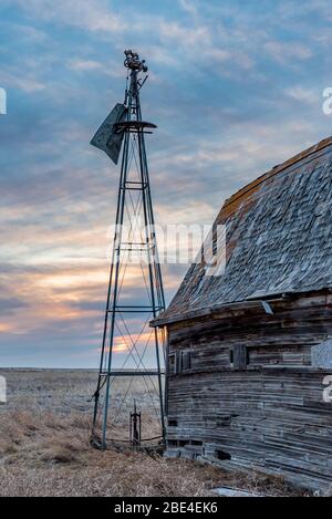 Coucher de soleil sur un moulin à vent d'époque cassé à côté d'une ancienne grange dans les Prairies en Saskatchewan Banque D'Images