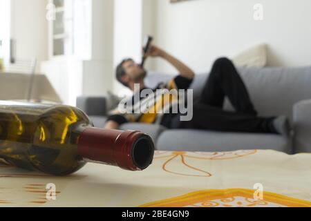 L'alcoolique est bu sur le canapé à la maison en arrière-plan. Bouteille de vin vide au premier plan. Concept d'alcoolisme familial. Banque D'Images