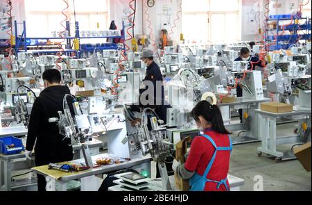 Qingdao, Chine. 11 avril 2020. Les travailleurs travaillent en heures supplémentaires pour produire du matériel d'étanchéité pour les vêtements de protection à l'atelier de Nawon Machinery Co., Ltd. Dans le district de Jimo de Qingdao, dans la province de Shandong en Chine orientale, le 11 avril 2020. Depuis sa reprise de la production le 7 février, Nawon Machinery Co., Ltd., investi en Corée du Sud, produit à pleine vitesse l'équipement d'étanchéité de joints pour les vêtements de protection, un équipement nécessaire mais non fabriqué en masse qui a été en court approvisionnement en raison de la propagation mondiale de la pandémie COVID-19. Crédit: Xinhua/Alay Live News Banque D'Images