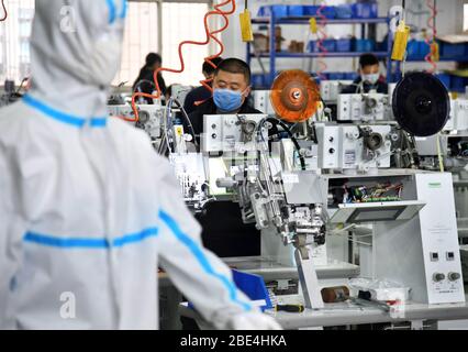 Qingdao, Chine. 11 avril 2020. Les travailleurs travaillent en heures supplémentaires pour produire du matériel d'étanchéité pour les vêtements de protection à l'atelier de Nawon Machinery Co., Ltd. Dans le district de Jimo de Qingdao, dans la province de Shandong en Chine orientale, le 11 avril 2020. Depuis sa reprise de la production le 7 février, Nawon Machinery Co., Ltd., investi en Corée du Sud, produit à pleine vitesse l'équipement d'étanchéité de joints pour les vêtements de protection, un équipement nécessaire mais non fabriqué en masse qui a été en court approvisionnement en raison de la propagation mondiale de la pandémie COVID-19. Crédit: Xinhua/Alay Live News Banque D'Images