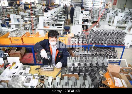 Qingdao, Chine. 11 avril 2020. Les travailleurs travaillent en heures supplémentaires pour produire du matériel d'étanchéité pour les vêtements de protection à l'atelier de Nawon Machinery Co., Ltd. Dans le district de Jimo de Qingdao, dans la province de Shandong en Chine orientale, le 11 avril 2020. Depuis sa reprise de la production le 7 février, Nawon Machinery Co., Ltd., investi en Corée du Sud, produit à pleine vitesse l'équipement d'étanchéité de joints pour les vêtements de protection, un équipement nécessaire mais non fabriqué en masse qui a été en court approvisionnement en raison de la propagation mondiale de la pandémie COVID-19. Crédit: Xinhua/Alay Live News Banque D'Images