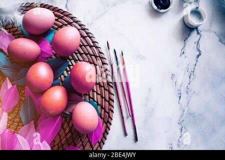 Fond coloré de pâques printanière avec des œufs violets colorés, des plumes blanches, des teintures, des brosses sur une table en marbre clair. Espace de copie, vue de dessus. Bonne fête de Pâques Banque D'Images