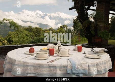 Table de petit-déjeuner située sur une terrasse avec vue, avec la chaîne de montagnes Annapurna dans l'Himalaya, dans un complexe de luxe à Pokhara, au Népal Banque D'Images