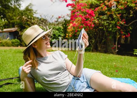 Une jeune femme souriante se couche sur une pelouse verte sous le soleil de l'été, tenez le smartphone connecté par usb à la banque d'alimentation portable Banque D'Images