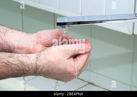 un homme se lave les mains avec du savon et de l'eau sous le robinet dans la salle de bains Banque D'Images