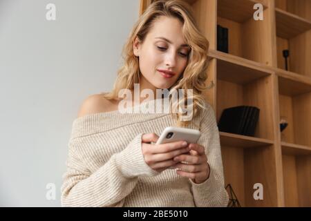 Image d'une jeune femme concentrée et belle à l'intérieur à la maison avec téléphone mobile. Banque D'Images