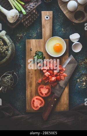 Tomates et œufs sur planche à découper en bois avec couteau sur fond sombre rustique de table de cuisine. Ingrédients de cuisine Shakshuka. Vue de dessus. Alimentation saine ea Banque D'Images