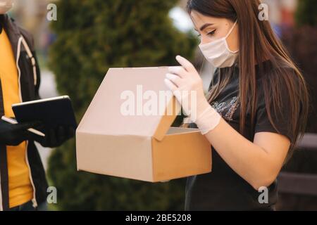 Homme du service de livraison dans le masque médical et gants de la remise de nourriture fraîche à la jeune femme client recevant la livraison express de coursier à la maison Banque D'Images