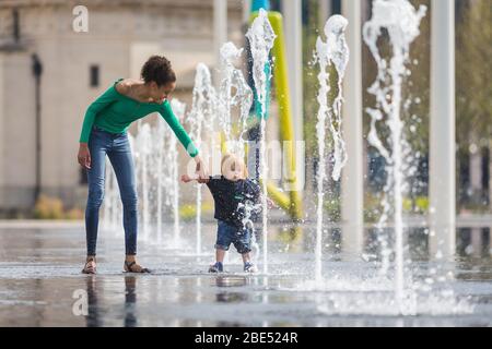 Birmingham, Royaume-Uni. 12 avril 2020. Mia, 12 ans, emmène son frère de 18 mois Jasper pour leur promenade d'exercice quotidien à travers les fontaines de la place du Centenaire, au centre-ville de Birmingham. Leur famille vit à proximité. Le dimanche de Pâques a commencé comme une journée chaude et ensoleillée. [Autorisation parentale accordée] crédit: Peter Lopeman/Alay Live News Banque D'Images