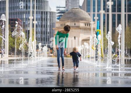 Birmingham, Royaume-Uni. 12 avril 2020. Mia, 12 ans, emmène son frère de 18 mois Jasper pour leur promenade d'exercice quotidien à travers les fontaines de la place du Centenaire, au centre-ville de Birmingham. Leur famille vit à proximité. Le dimanche de Pâques a commencé comme une journée chaude et ensoleillée. [Autorisation parentale accordée] crédit: Peter Lopeman/Alay Live News Banque D'Images