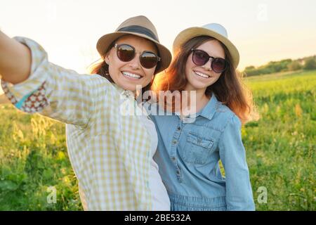 Bonne mère souriante et fille de l'adolescence prenant la photo de selfie. Les femmes marchent dans les prairies le jour ensoleillé de l'été. Relation parent-enfant Banque D'Images