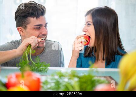 Un couple heureux mangeant des fruits et des légumes pour le petit déjeuner du matin - jeunes préparant un repas sain à la maison pendant l'isolement de quarantaine - foyer principal Banque D'Images