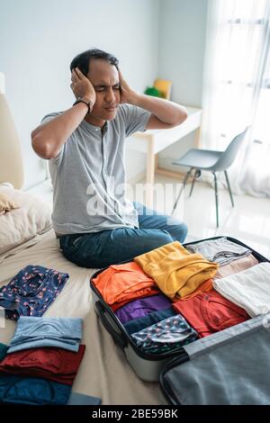 jeune homme stressé après avoir reçu une annulation de billet de vol lors de la préparation de ses vêtements dans la valise avant d'aller à long voyage Banque D'Images