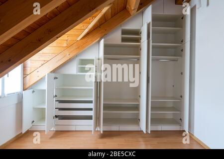 Vue intérieure d'un placard sur mesure avec portes ouvertes intégrées dans une chambre principale avec toit en pente Banque D'Images