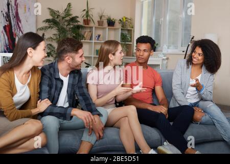 Passer du temps avec vos amis. Groupe de jeunes multiculturels dans une tenue décontractée parler et se reposer ensemble tout en assis sur le canapé à la maison. Ils Banque D'Images